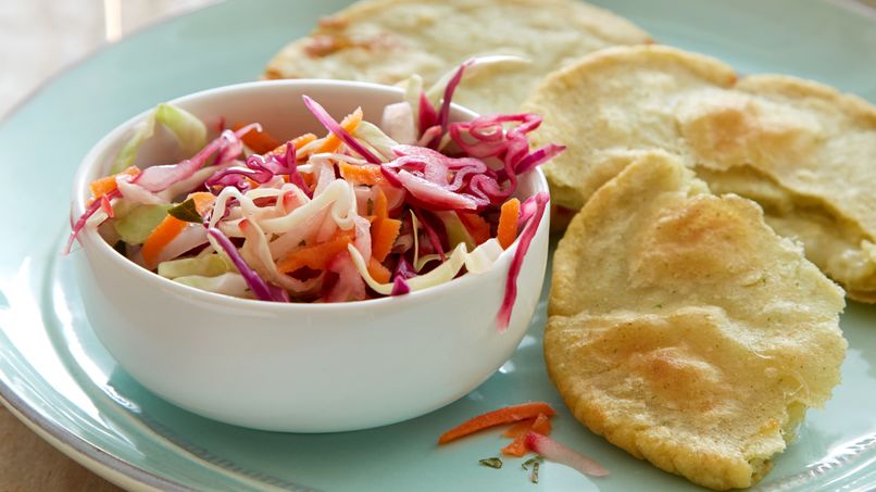 Tres pupusas de queso, una abierta por la mitad, en un plato verde claro con un plato de repollo blanco y morado rallado, zanahorias y rábanos.